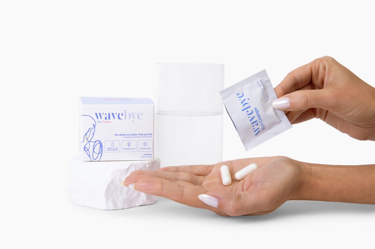 Two hands holding a white Wavebye Bye Cramps box with blue branding against a white background