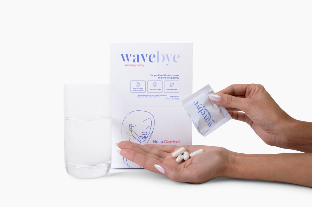 Hands holding a Wavebye Bye Irregularity packet and box with pills displayed on a white background