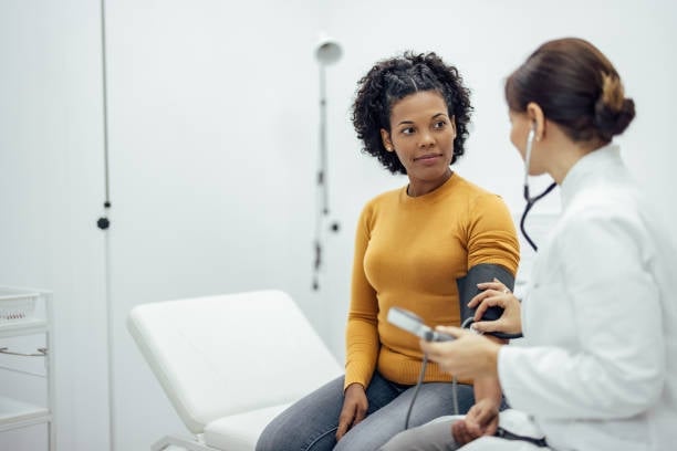 A female doctor in a white coat using a stethoscope to examine a patient in a yellow shirt in a medical clinic, the patient looking directly at her, the kind of appointment where she is heard