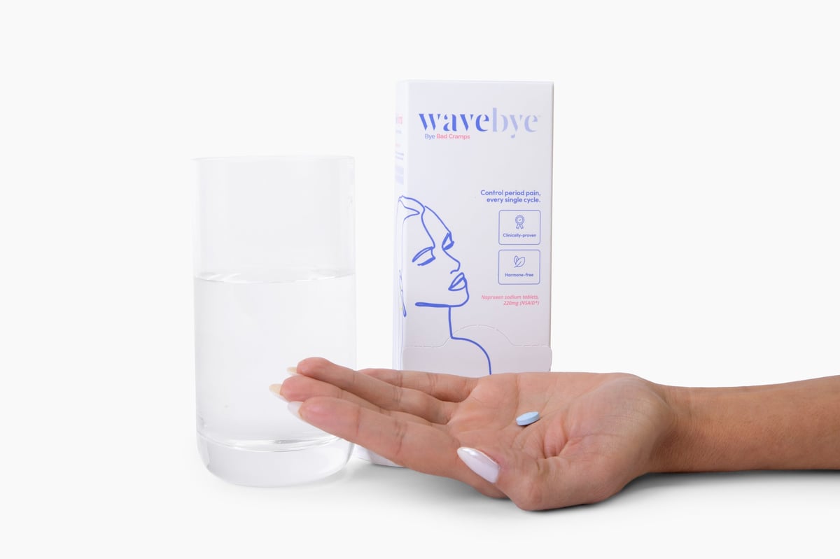 Hand holding a Wavebye Bye Bad Cramps box next to a clear glass bottle on a white background